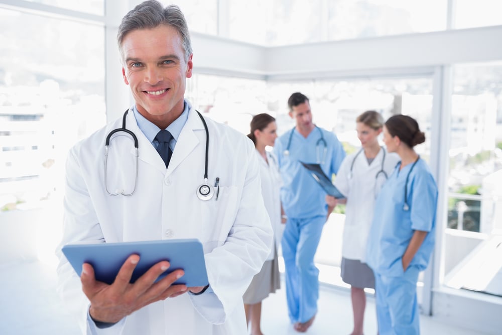 Smiling doctor holding digital tablet in front of his medical team